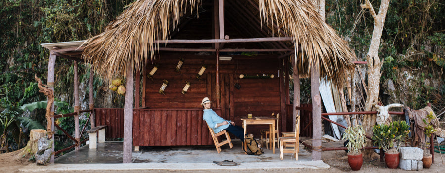 A man on a rocking chair in a grass shack in Cuba.