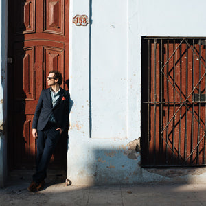 A man leaning against a wall in Cuba wearing a casual suit.
