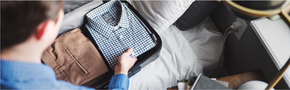 An overhead view of a suitcase packed with nicely folded dress shirts and pants.