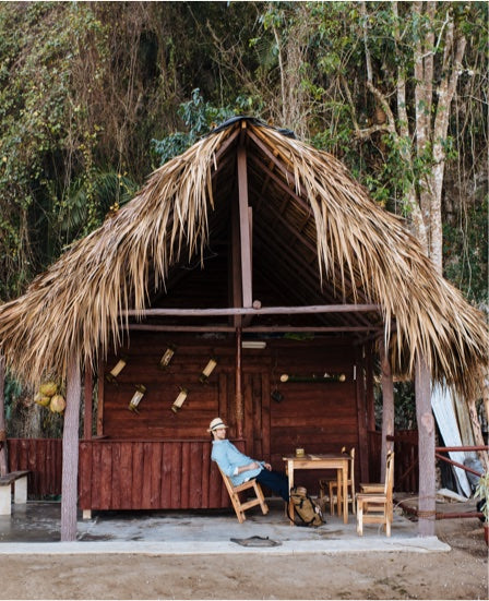 A man on a rocking chair in a grass shack in Cuba.