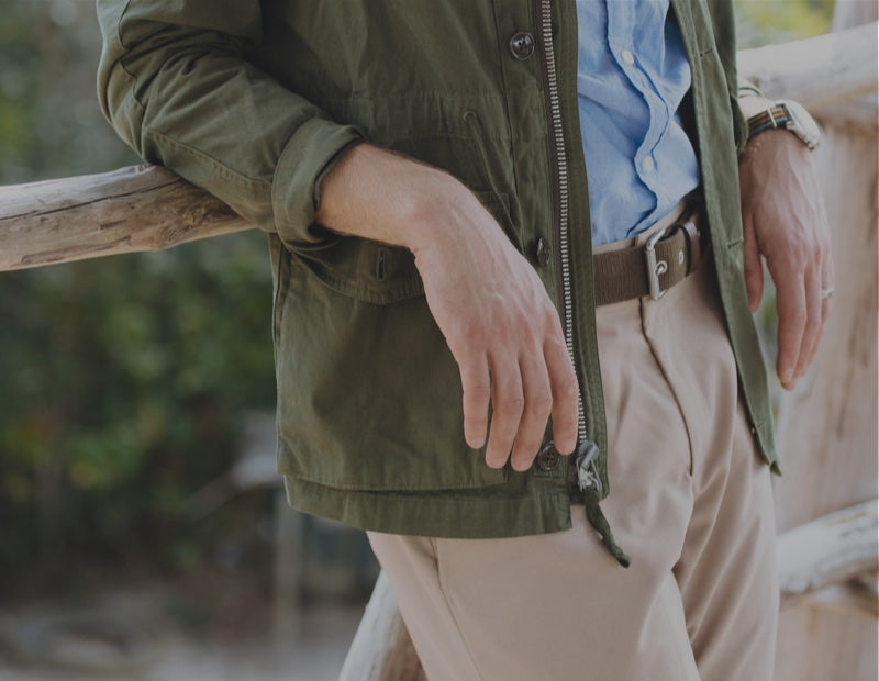 A detail of a green work jacket, blue button down, and khakis in a hot climate.